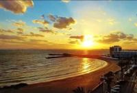 a sunset on a beach with the ocean and buildings at 100 m de la plage - Les Cigales de Mer - Studio Cabine - Parking in Le Grau-du-Roi