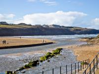 a beach with people walking on the sand and water at Quay House, Porth Beach in Saint Columb Minor