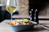 Un bol de ensalada junto a una copa de vino blanco en The Coach House, en Potton