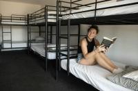 a woman sitting on a bunk bed reading a book at Nomads St Kilda in Melbourne