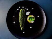 a black plate with a pickle and a vegetable on it at Auberge Les Grillons in Meyras