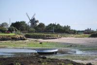 a boat on the shore with a windmill in the background at Hotel au Moyne De Saire in Réville