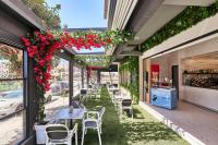 un patio con mesas, sillas y flores rojas en Stay 365 Heraklion Apart Hotel, en Heraclión