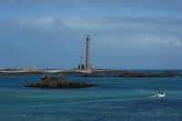 a boat in the water with a lighthouse in the background at Kerletty, la mer, les embruns, à 250 m des plages in Plouguerneau