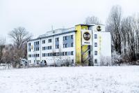 a building in the snow with a field in front of it at B&B HOTEL München-Airport in Hallbergmoos