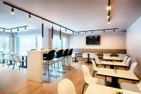 a restaurant with white tables and chairs and a tv on the wall at B&B HOTEL München-Airport in Hallbergmoos