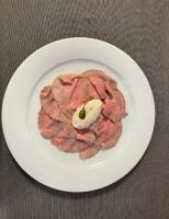 Un plato blanco con un trozo de carne con un pepinillo encima. en Hotel Il Grappolo D'Oro, en Monforte dʼAlba