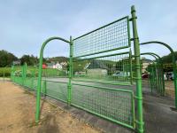 a green metal fence with a tennis court at Maison Village de La Verrerie in Cherbourg en Cotentin