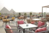 a patio with tables and chairs with pyramids in the background at New Pyramid Front Hotel in Cairo