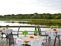 Dos mesas con manteles blancos en una terraza con vista al río. en Gondwana Hakusembe River Lodge, en Rundu