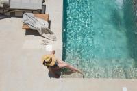 Una mujer con sombrero sentada junto a una piscina. en Muses of art Villas, en Afantou