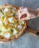 Una mano se extiende hacia una pizza sobre una tabla de madera. en The Hong C Hotel, en Gangneung