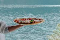una persona sosteniendo una pizza en un plato cerca del agua en Briisa De Ness, en Nesso