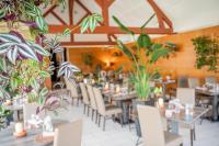 Un comedor con mesas y sillas y plantas. en Logis Hostellerie la Chaumière, en Arsonval