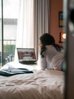 a woman sitting on a bed using a laptop computer at Deskopolitan House in Paris