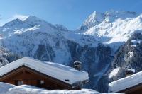a house covered in snow with mountains in the background at Chataigne, cosy 3 bedroom apartment with great views in Sainte-Foy-Tarentaise