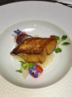 a white plate with a piece of fish on rice at Chateau Le Prieuré Saumur - La Maison Younan in Chènehutte-les-Tuffeaux