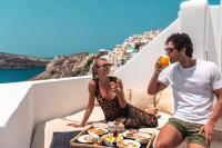 a man and woman sitting on a balcony drinking orange juice and eating food at Aspaki by Art Maisons in Oia