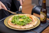 una persona cortando una pizza con un cuchillo y un tenedor y una botella de cerveza en Hôtel Esté, en París