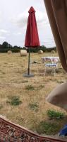 a red umbrella and chairs in a field at La tente saharienne du Perche .Chevaux. 