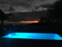 a blue swimming pool with a sunset in the background at Cocooning Tropic Studio avec Jacuzzi privatif in Saint-Louis