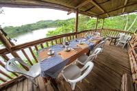 una mesa y sillas en una terraza con vistas al río en Dave the Cave Eco Lodge and Cultural Campsite, en Rubirizi