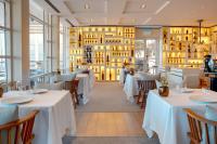 Un restaurante con mesas y sillas blancas y ventanas. en Hotel Arts Barcelona, en Barcelona