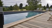 a swimming pool with a wooden deck and chairs at Une pause en Corrèze in Sarroux