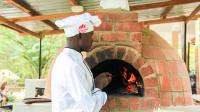 um chef em pé em frente a um forno de tijolos em Bunyonyi Safaris Resort em Kabale