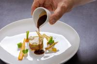 Eine Person schüttet Soße in einen Teller Essen. in der Unterkunft Wellness & Naturresort Reischlhof in Wegscheid