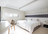 a white bedroom with a large bed and a chair at Dandy Hotel - Tianmu Branch in Taipei
