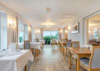 a restaurant with white tables and chairs and windows at Beacon Country House Hotel &amp; Luxury Shepherd Huts in St. Agnes