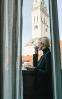 a woman drinking a coffee while looking out a window with a clock tower at Louis Hotel in Munich