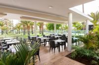 Un restaurante con mesas y sillas y palmeras. en Hotel Riu Gran Canaria - All Inclusive, en Maspalomas