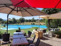 eine Gruppe von Tischen und Stühlen mit Sonnenschirmen und einem Pool in der Unterkunft L'Oasienne in Lissac et Mouret