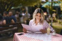 una mujer sentada en una mesa leyendo un periódico en Wood Mood Apartman Tiganjica, en Staji°evo