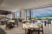 HUALUXE Sanya Yalong Bay Resort في سانيا: مطعم به طاولات وكراسي ونوافذ كبيرة