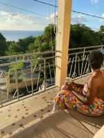 a woman sitting on a balcony looking out at the ocean at Télétravail et Plaisir au soleil avec vue mer! in Bouillante