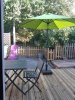 a green umbrella sitting on a wooden deck with a chair and a table at Au ptit Manoir in Montbert