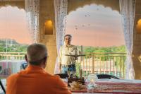 een man die een bord vasthoudt voor een man die aan een tafel zit bij Hotel Meri Haveli in Jaisalmer