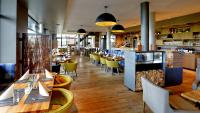 un restaurante con mesas de madera y sillas amarillas en Elbstrand Resort Krautsand - Hotel Elbstrand, en Drochtersen