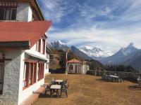 Un edificio con mesas y sillas y montañas al fondo. en Sherpa Panorama Hotels, en Khumjung