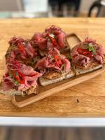 Un plato de madera con tres rebanadas de pan con carne. en Penzion pod Hazmburkem, en Klapý