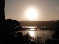 a bridge over a river with the sun in the background at château de Locquéran Pierres et filets bleus in Plouhinec
