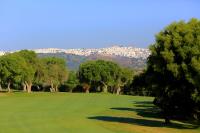 a golf green with trees and a city in the background at Hotel Hacienda Montenmedio in Vejer de la Frontera