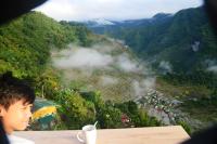 Un niño sentado en una mesa mirando un valle montañoso. en Batad Roberto's Abung Inn and Restaurant, en Banaue
