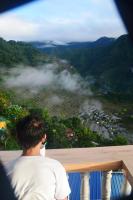 Un hombre sentado en una barandilla mirando una montaña. en Batad Roberto's Abung Inn and Restaurant, en Banaue