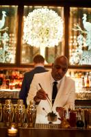a man in a white suit and tie holding a pen in a bar at The Fifth Avenue Hotel in New York