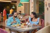 a man and woman sitting at a table in a restaurant at Flora Airport Hotel and Convention Centre Kochi in Nedumbassery