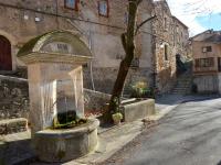 a stone fountain on the side of a street at L&#39;Armandière, maison de caractère où règne calme et sérénité. in Pézenes-les-Mines